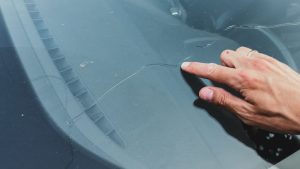 man's hand pointing at a long crack on a car windshield,